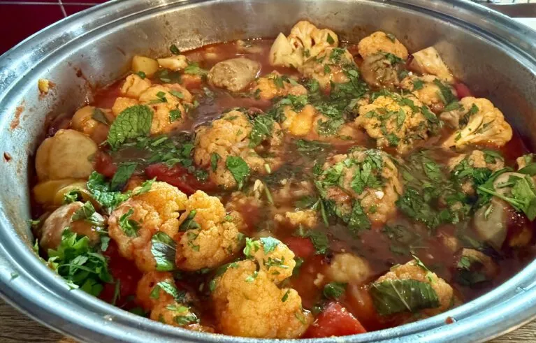 picturre of braised cauliflower in a red based sauce, sprinkled with chopped green parsley