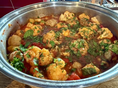 picturre of braised cauliflower in a red based sauce, sprinkled with chopped green parsley