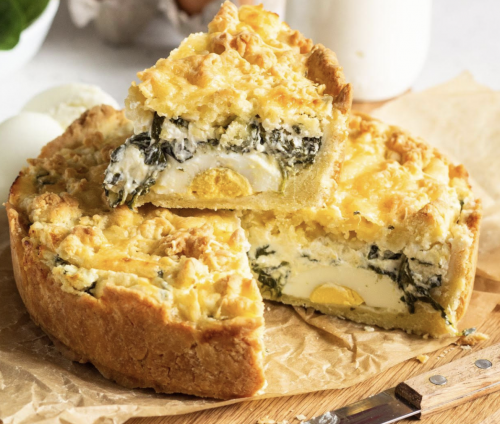 Torta Pasqualina, on a wooden board, cut open to show the spinach, eggs and ricotta.